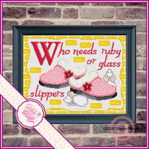 May include: Cross-stitch art in a black frame features the text "Who needs ruby or glass slippers" above a pair of pink slippers with white trim and red flower accents. A white mouse is next to the slippers. The artwork is on a white background with yellow accents.