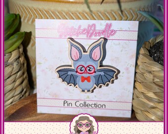 May include: A wooden pin featuring a gray bat with large ears, pink inner ears, red glasses, and a red bowtie. The pin is attached to a white display card with the text StitchDoodle Pin Collection and a small illustration of a person with glasses.