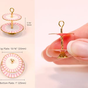 May include: A miniature two-tier cake stand with pink and white striped plates and a gold-tone metal center post. The total height is 1 1/4 inches, with a 7/16 inch tier gap. The top plate is 13/16 inches and the bottom plate is 1 inch wide.