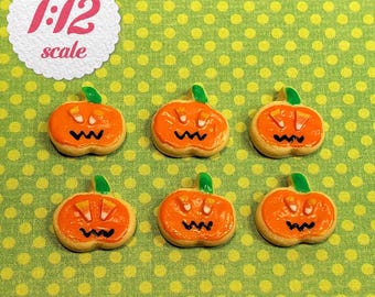 May include: Six miniature pumpkin-shaped cookies in 1:12 scale, each featuring orange icing, two candy corn eyes, and a black zigzag mouth. The cookies are arranged in two rows of three, showcasing a consistent design with green stems.