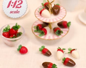 May include: A 1:12 scale miniature two-tier serving stand with pink and white striped plates, holding chocolate-dipped strawberries. A small glass bowl contains fresh strawberries, and additional chocolate-dipped strawberries are scattered nearby.