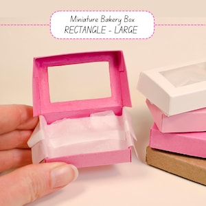 May include: A pink miniature bakery box with a rectangular window, open to reveal white tissue paper. The text "Miniature Bakery Box RECTANGLE - LARGE" is above the box. Other boxes are stacked nearby.