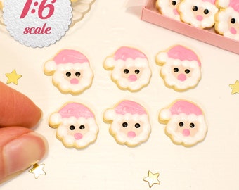 May include: Six pink and white Santa Claus cookies with black eyes and a pink nose. The cookies are arranged in two rows of three on a white surface. The cookies are 1:6 scale.