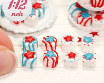 May include: A collection of miniature red, white, and blue decorated cakes with star designs. The cakes are arranged on a white surface and are 1/12 scale.