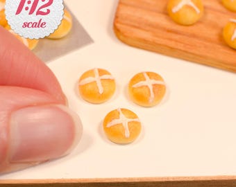 May include: Miniature 1:12 scale hot cross buns featuring golden brown dough with a white icing cross pattern. These small baked goods are arranged on a flat surface near a wooden board, showcasing a realistic texture and detailed miniature design.