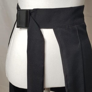 May include: A black wrap skirt with a black adjustable buckle belt. The skirt has a front slit and is made of a smooth fabric.