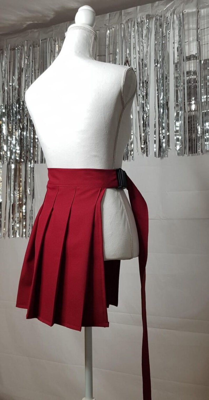 May include: A red pleated skirt with a black adjustable buckle belt. The skirt has a side slit and a long tie that can be worn as a belt.