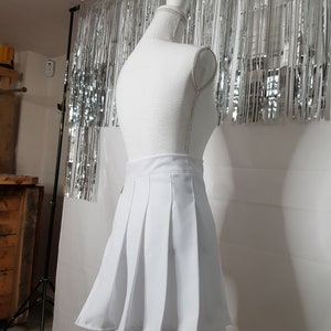 May include: A white pleated skirt on a white mannequin. The skirt is short and has a high waist.
