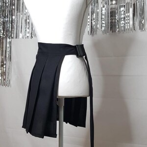 May include: A black pleated skirt with a long tie that can be worn as a belt. The skirt has a side slit and is displayed on a white mannequin.