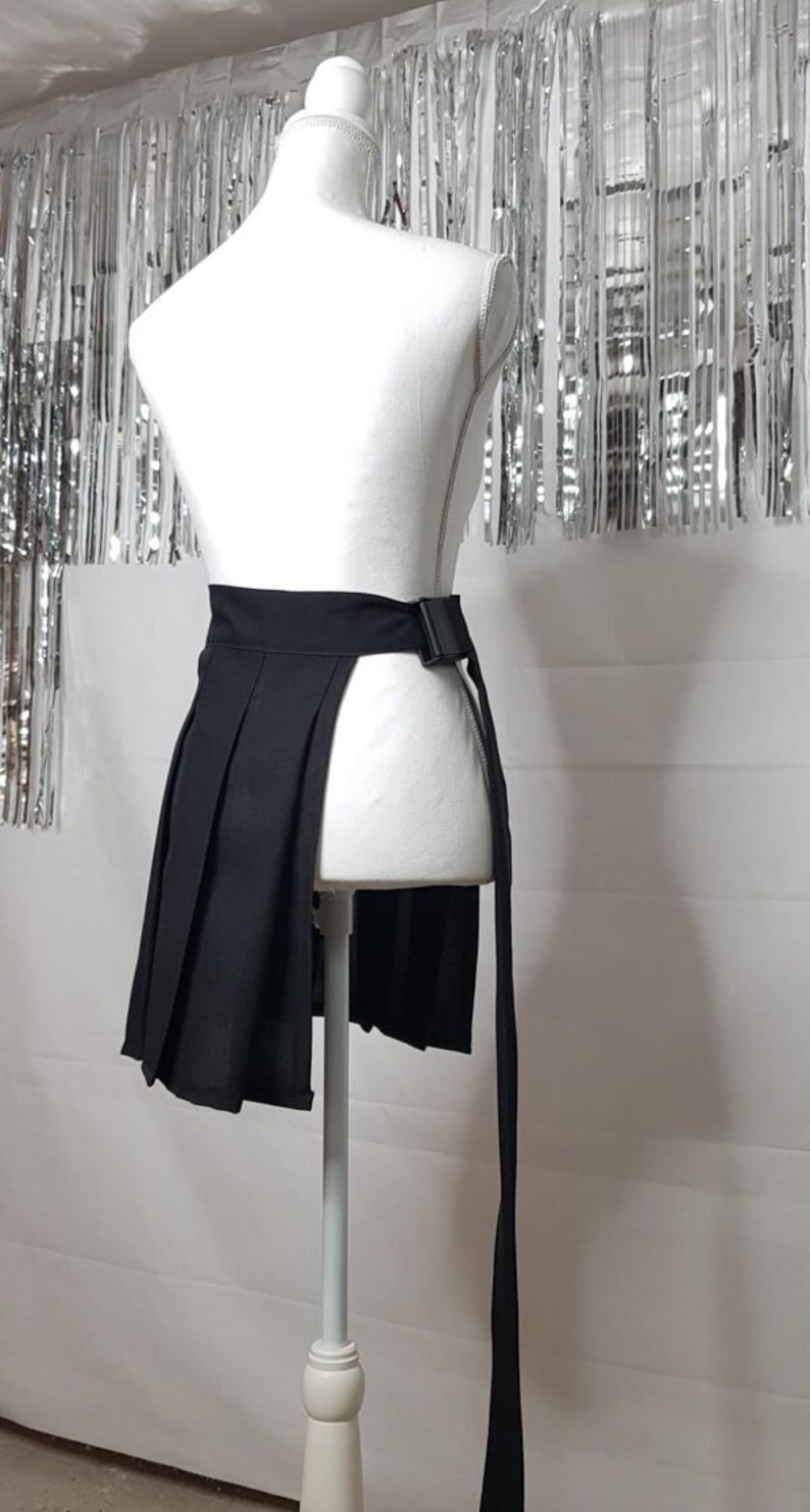 May include: A black pleated skirt with a long tie that can be worn as a belt. The skirt has a side slit and is displayed on a white mannequin.
