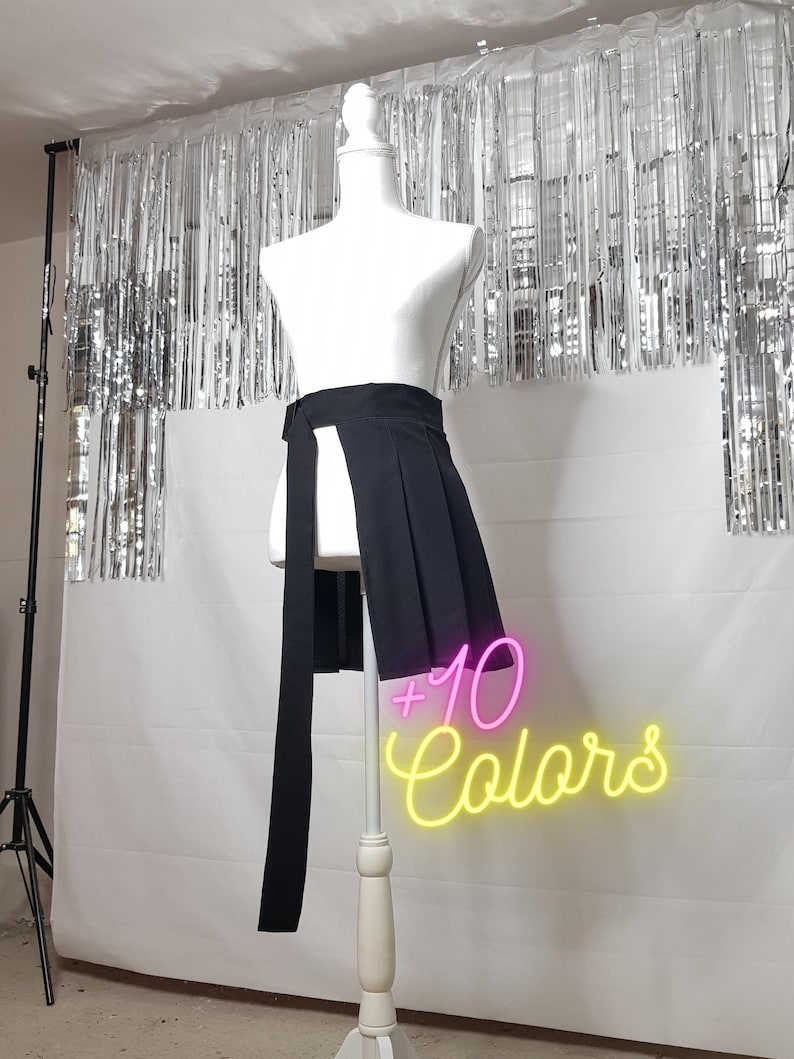 May include: A black skirt with a high waist and a long, asymmetrical front panel. The skirt is pleated and has a tie at the waist. The text '+10 Colors' is visible in the image.