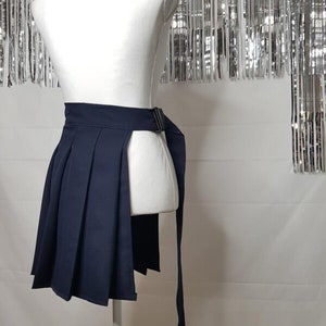 May include: A navy blue pleated skirt with a side slit and a long tie belt. The skirt is on a white mannequin.