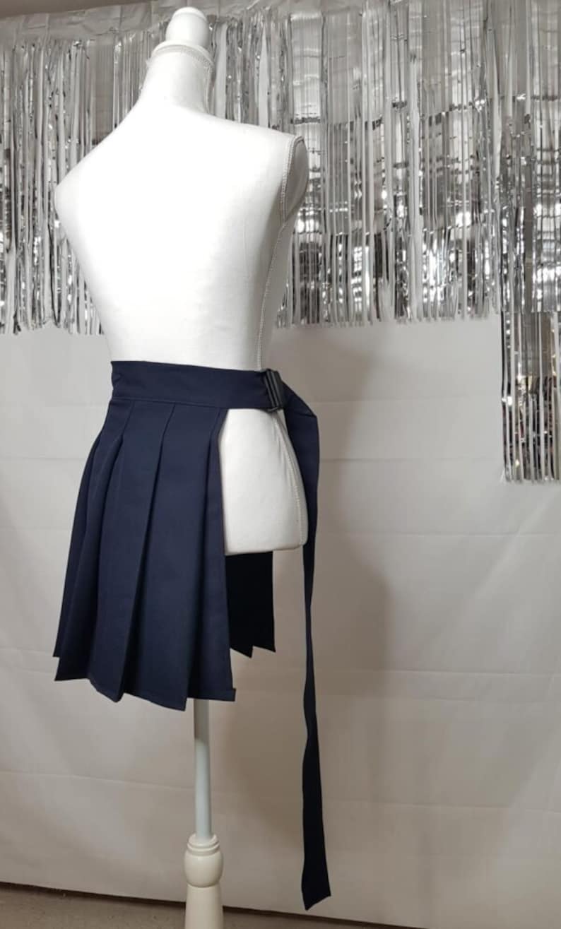 May include: A navy blue pleated skirt with a side slit and a long tie belt. The skirt is on a white mannequin.