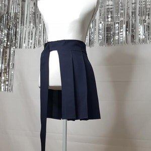 May include: A navy blue pleated skirt with a long tie that wraps around the waist. The skirt has a slit in the front and is displayed on a white mannequin.