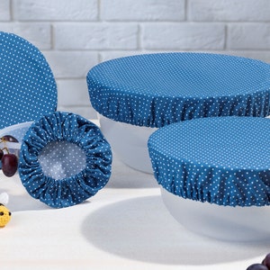 Könnte beinhalten: Vier blaue und weiße gepunktete Stoff-Schüssel-Abdeckungen. Die Abdeckungen bestehen aus einem dehnbaren Stoff und können verwendet werden, um Schüsseln unterschiedlicher Größe abzudecken. Die Abdeckungen befinden sich auf weißen Schüsseln und einer weißen Oberfläche.