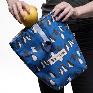 May include: A blue reusable lunch bag with a penguin pattern and the text "It is cool man".