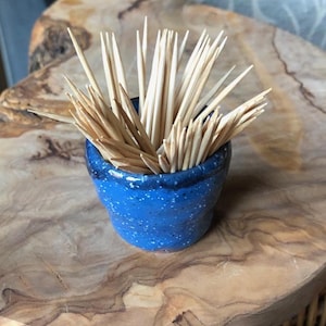 Könnte beinhalten: Ein blauer Keramik-Zahnstocherhalter mit weißen Punkten, gefüllt mit Holz-Zahnstochern.