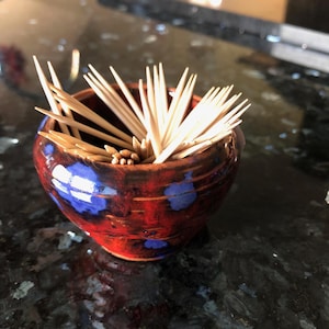 May include: A red and blue ceramic toothpick holder filled with wooden toothpicks.