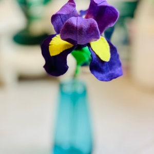 May include: A purple and yellow felt flower in a blue vase. The flower is a felt craft.