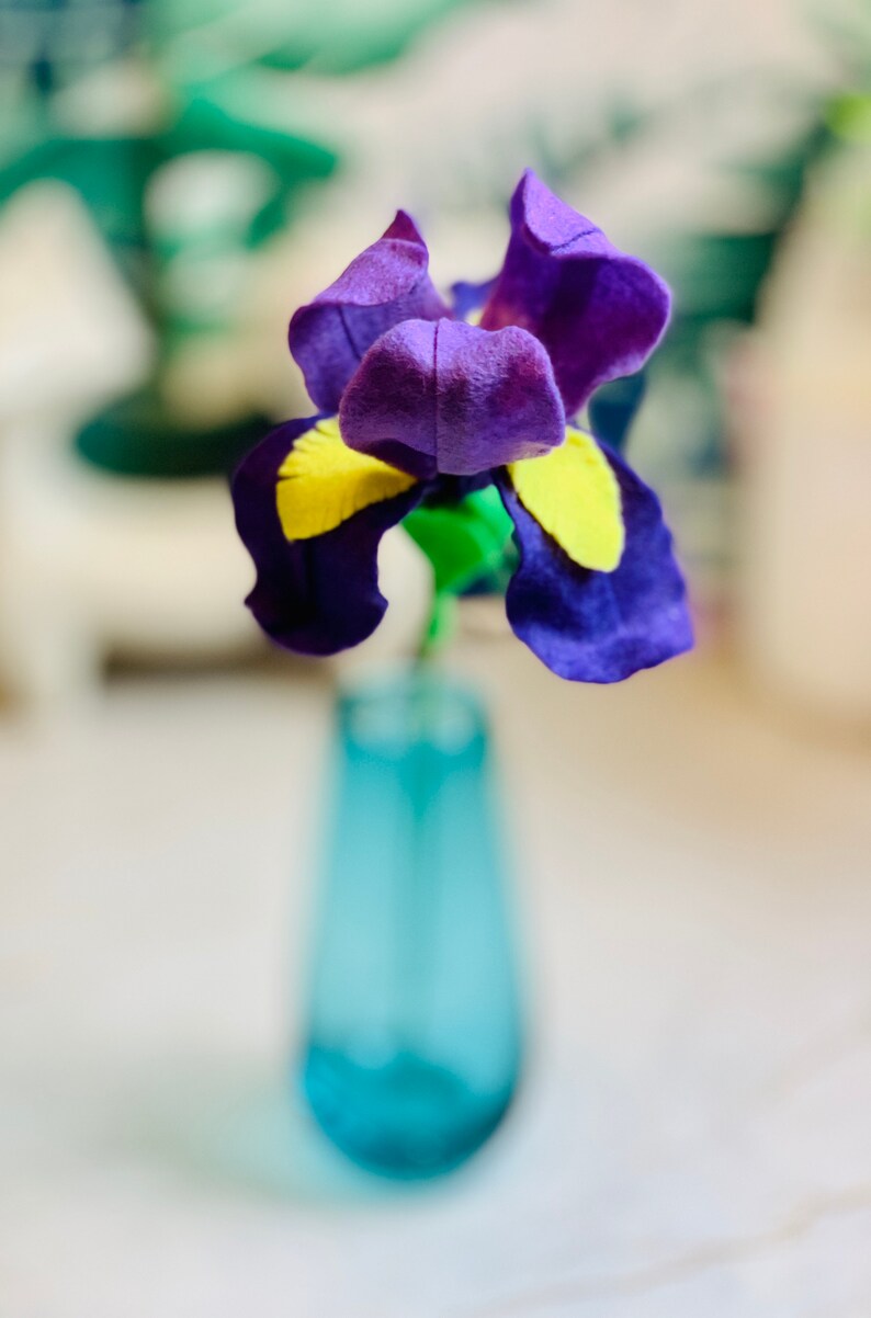 May include: A purple and yellow felt flower in a blue vase. The flower is a felt craft.