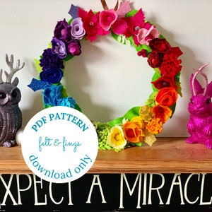 May include: A rainbow felt flower wreath with green leaves and a white circle with the text "PDF PATTERN felt & fings download only".