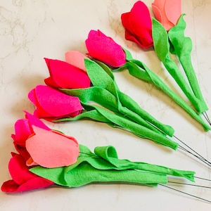 Könnte beinhalten: Ein Strauß aus Filz-Tulpen mit rosa und roten Blütenblättern und grünen Stielen. Die Tulpen sind in einer Reihe angeordnet, wobei die Stiele nach rechts zeigen.
