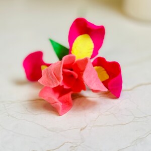 May include: A pink and yellow felt flower with a green stem. The flower has a layered design with multiple petals.