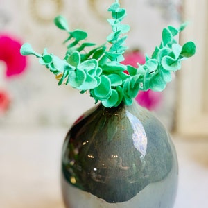 May include: A light green felt eucalyptus plant in a dark gray ceramic vase with a glossy finish.