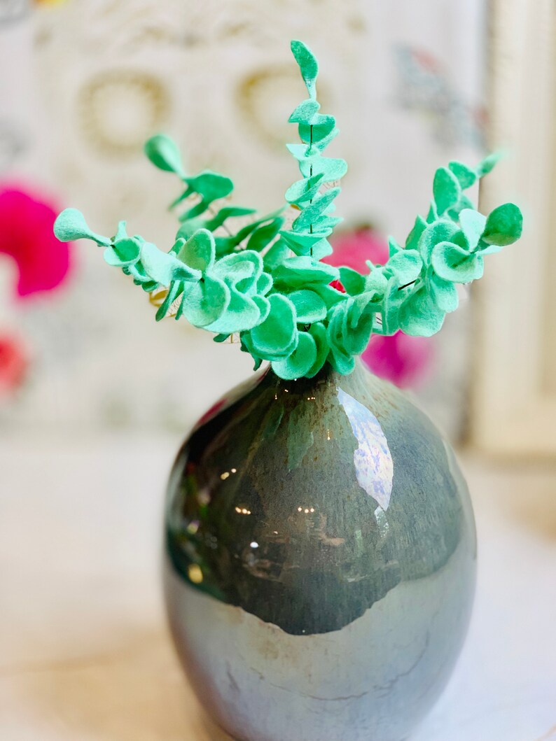 May include: A light green felt eucalyptus plant in a dark gray ceramic vase with a glossy finish.