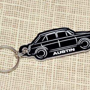 May include: Black and white metal keychain featuring a silhouette of a car with the word "AUSTIN" printed on the side. The keychain has a silver ring.