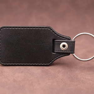Rear of the medallion keyring with black leatherette fob on a brown suede background.