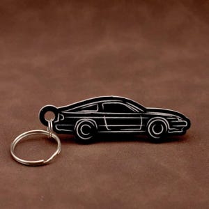 Op de afbeelding: Zwarte autosleutelhouder met een zilveren sleutelring. De auto is een zijaanzicht van een coupé.