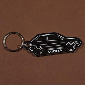 Pode incluir: Chaveiro preto e branco em forma de carro Nissan Micra. O chaveiro tem um anel de metal prateado.