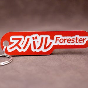 Peut inclure: Porte-clés rouge et blanc avec le texte "Subaru Forester" en lettres blanches. Le porte-clés est en métal et possède un anneau de clé argenté.