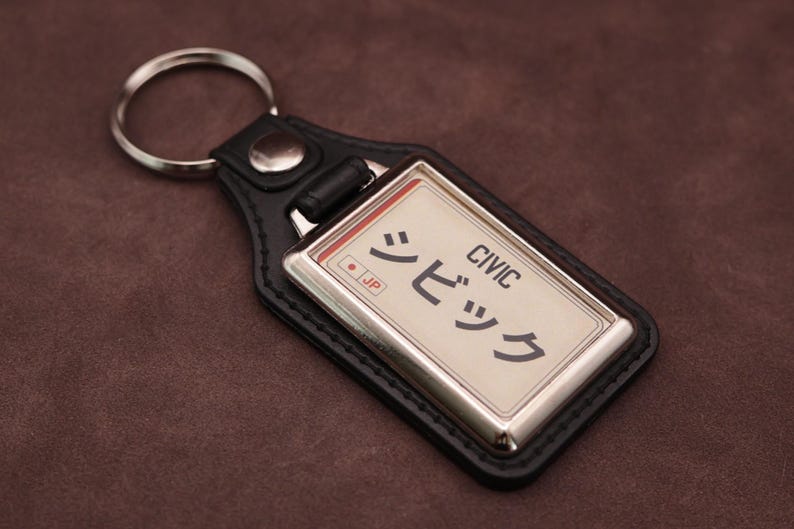 Honda Civic Japanese plate medallion keyring with black leatherette fob, chrome frame and cream insert on a brown suede background.