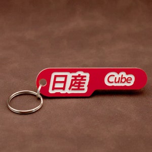 May include: Red keychain with a silver ring and the text "Cube" and Japanese characters.