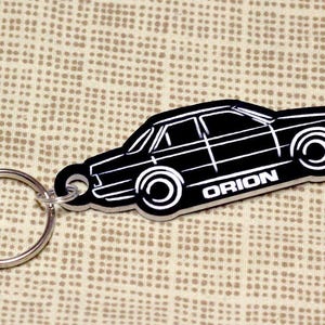 Peut inclure: Porte-clés en métal noir avec une silhouette de voiture et le mot "ORION" imprimé en bas.