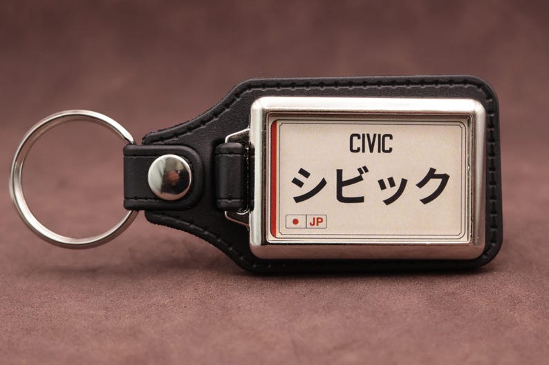 Honda Civic Japanese plate medallion keyring with black leatherette fob, chrome frame and cream insert on a brown suede background.