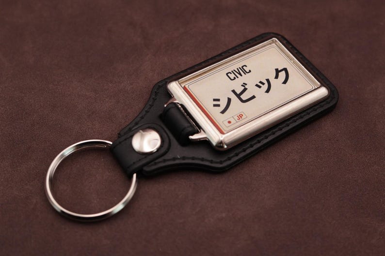 Honda Civic Japanese plate medallion keyring with black leatherette fob, chrome frame and cream insert on a brown suede background.
