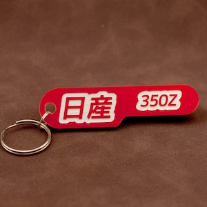 Op de afbeelding: Rode sleutelhanger met een witte inscriptie die "日輪 350z" luidt.