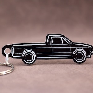 May include: Black and white outline of a pickup truck keychain. The keychain is made of metal and has a silver key ring.