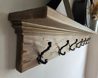 May include: A wooden shelf with a decorative trim and multiple black metal hooks. The shelf is stained a dark brown color and has a rustic appearance.