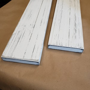 May include: Two white wooden shelves with a distressed finish. The shelves have a dark gray border around the edges.