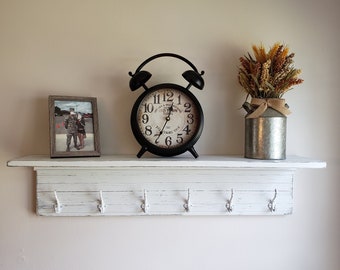 May include: White shelf with five hooks, a black alarm clock with a white face, and a framed photo. The clock face reads "Old Town Clock" and has a vintage look. The shelf is distressed and has a rustic look.