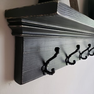 May include: Black wooden shelf with a decorative trim and five black metal hooks. The shelf is distressed and has a rustic look.