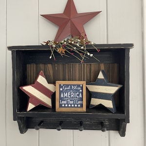 May include: Black wooden shelf with three hooks, decorated with red, white, and blue stars and a sign that reads "God Bless America Land That I Love".