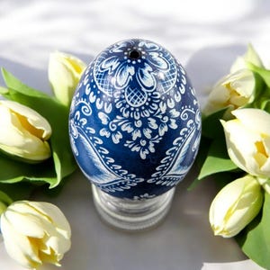 Può includere: Un uovo di Pasqua blu con un motivo floreale bianco, circondato da tulipani bianchi.