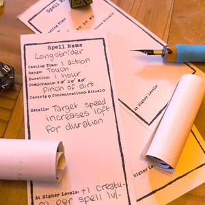 May include: A tabletop scene featuring role-playing game (RPG) elements. Includes dice, spell cards, an ink bottle, a pen, and rolled paper. The spell card text reads "Longstrider" and details about casting time, duration, and components.