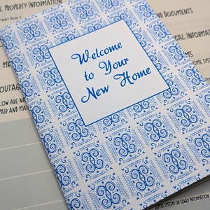 Puede incluir: Un folleto blanco con una cubierta de patrón azul y blanco. La cubierta tiene el texto "Bienvenido a su nuevo hogar" en letras azules.