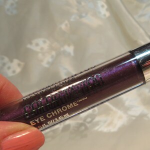 May include: A tube of eye makeup, labeled "Eye Chrome", with a metallic silver cap and a clear body revealing a deep purple liquid. The product is 0.11 fl oz / 3.45 ml.